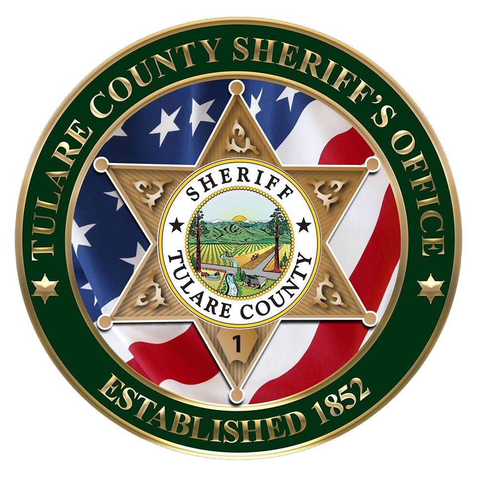 The Tulare County Sheriff's Office Challenge Coin is round with the 6-point Star in the middle on top of the stars and stripes of the American Flag. In the middle of the Tulare County Sheriff's Star is a scene of the sun rising over a valley with a river running down the center and tall redwood trees on both sides. The border around the coin is dark green with gold lettering "Tulare County Sheriff's Office" at the top and "Established 1852" on the bottom.