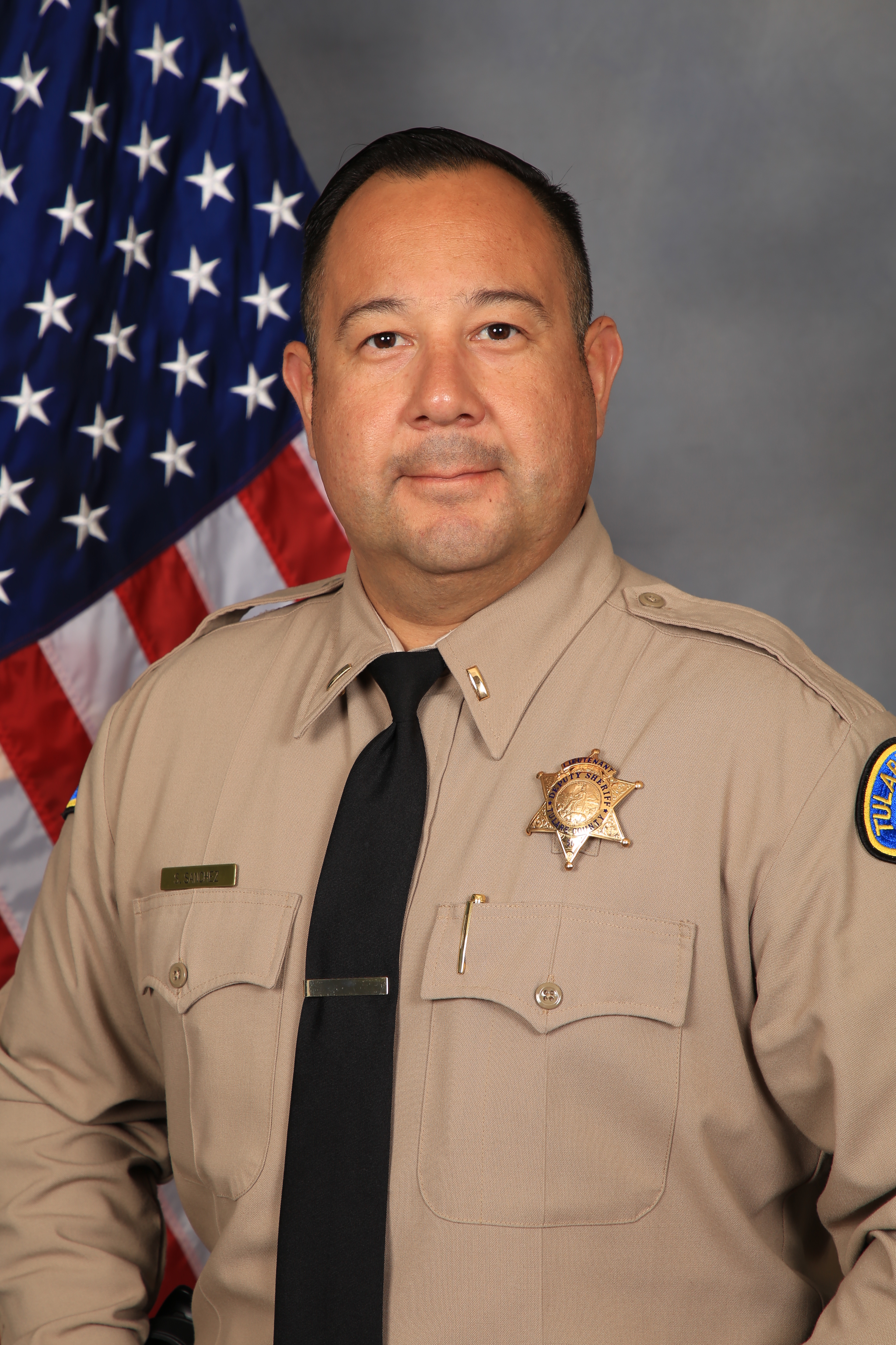 A head and shoulders portrait of Lt. Steve Sanchez in uniform in front of the American Flag.